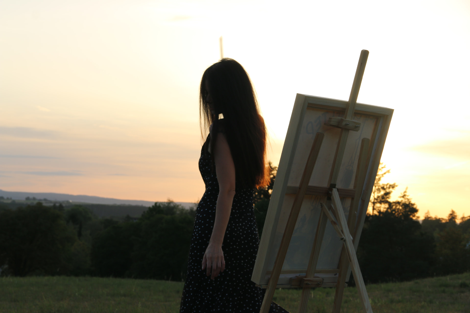 Alisa beside her easel in an open field at dusk